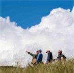 Clouds loom in the background as college students walk through tall beach grass on an outdoor classroom assignment.